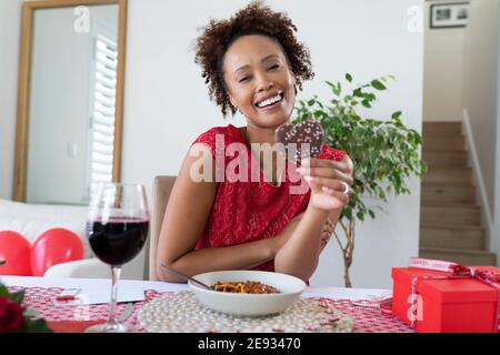 Portrait d'une femme afro-américaine tenant un cookie en forme de cœur vidéo à la maison Banque D'Images