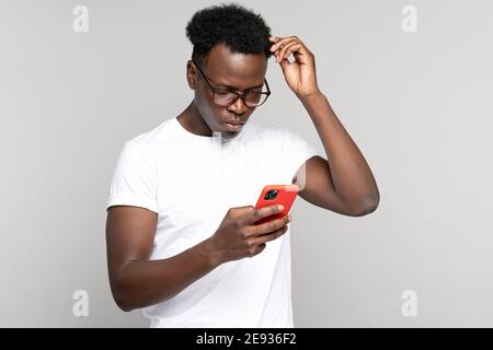 Pensive Afro homme se grattant la tête, regardant le téléphone mobile, pensant, planifie ou réexamine quelque chose Banque D'Images