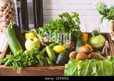 Blender et bouteilles devant un mur blanc, verts dans un coffret en bois. Pomme verte, citron, radis, persil, verger, menthe, marrows, avocat, kiwi, kohlr Banque D'Images