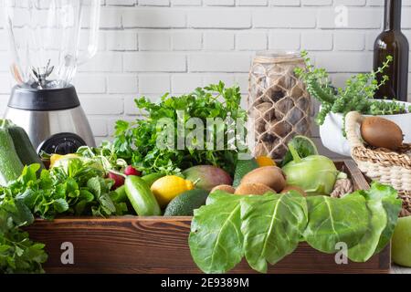 Blender et bouteilles devant un mur blanc, verts dans un coffret en bois. Pomme verte, citron, radis, persil, verger, menthe, marrows, avocat, kiwi, kohlr Banque D'Images
