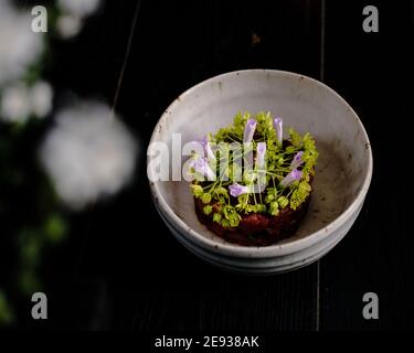 Tartare de viande rouge décorée et plaquée de fleurs et jardin vert Banque D'Images