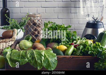 Blender et bouteilles devant un mur blanc, verts dans un coffret en bois. Pomme verte, citron, radis, persil, verger, menthe, marrows, avocat, kiwi, kohlr Banque D'Images