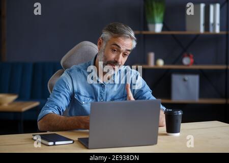 Portrait d'un homme aux cheveux gris, souriant et beau, travaillant à la maison. Communication en ligne avec des collègues et vidéoconférence. Réunion en ligne Banque D'Images