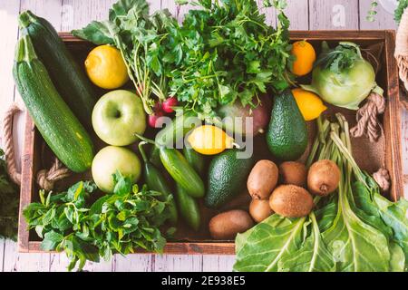 Blender et bouteilles devant un mur blanc, verts dans un coffret en bois. Pomme verte, citron, radis, persil, verger, menthe, marrows, avocat, kiwi, kohlr Banque D'Images