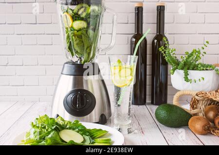 Blender et bouteilles devant un mur blanc, verts dans un coffret en bois. Pomme verte, citron, radis, persil, verger, menthe, marrows, avocat, kiwi, kohlr Banque D'Images