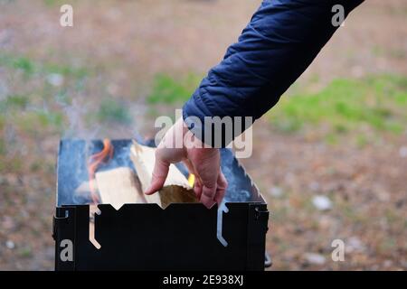 Allumer la grille. L'homme allume le feu pour griller. La main de l'homme ajoute du bois au feu. Banque D'Images