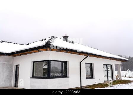 Toit d'une maison unifamiliale recouvert de neige sur un ciel nuageux. Cheminée visible, portes, fenêtres et chute de neige. Banque D'Images