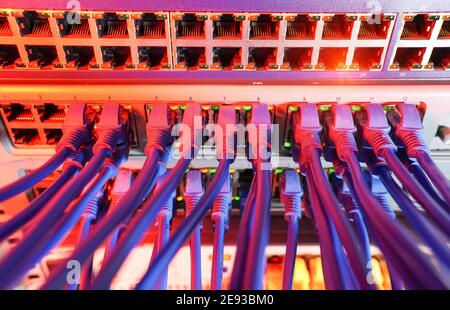 Rack serveur bleu et rouge avec cordon de raccordement internet câbles connectés au panneau de raccordement noir dans la salle des serveurs de données Banque D'Images
