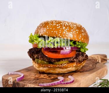 Hamburger juteux avec du bœuf, des tomates, des concombres et des oignons joliment agencés sur une planche de bois sur fond blanc Banque D'Images