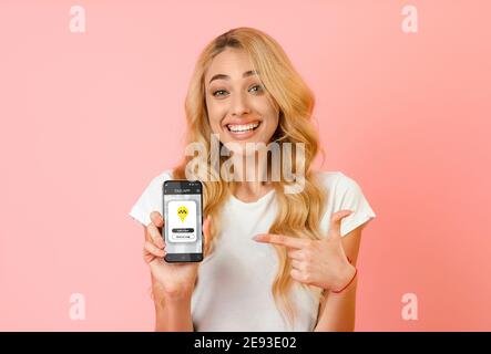Bonne femme pointant vers un smartphone avec l'application de taxi mobile à l'écran sur fond de studio rose. Concept de transport urbain Banque D'Images