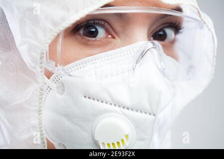Gros plan sur une infirmière ou un médecin terrifié du NHS britannique Porter un masque de protection EPI, des lunettes de protection, une combinaison propre, la peur et le stress yeux à échéance Banque D'Images