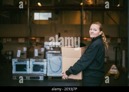 Femme d'affaires mature transportant un conteneur de boîte dans un entrepôt logistique Banque D'Images