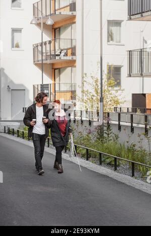 Femme malvoyante marchant dans la rue avec un ami masculin Banque D'Images