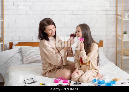 Soin beauté à la maison pour la mère et la fille. Une jeune femme et un jeune enfant heureux se curling les cheveux, ayant une journée de spa domestique Banque D'Images