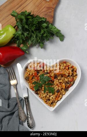 Ptitim de pâtes maison avec légumes sur une assiette en forme de cœur sur une table grise. Vue de dessus. Format vertical Banque D'Images
