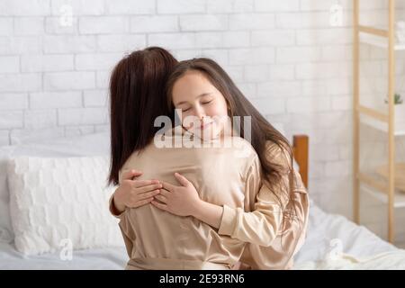 Une jeune fille affectueuse en forme d'oreille intime embrassant sa mère sur son lit à l'intérieur. Construire de solides relations familiales concept Banque D'Images