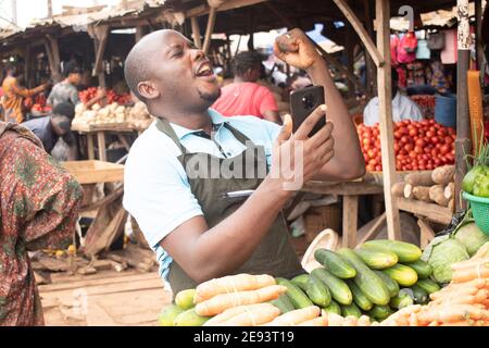 un homme célèbre sur le marché tout en tenant son téléphone avec sa main droite Banque D'Images