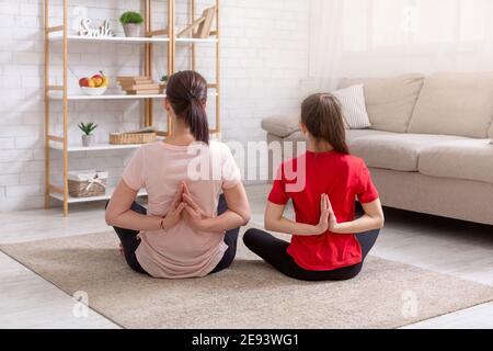 Vue arrière de la mère et de la fille assis dans la posture du lotus, faisant un geste namaste, faisant la pratique du yoga du matin ensemble Banque D'Images