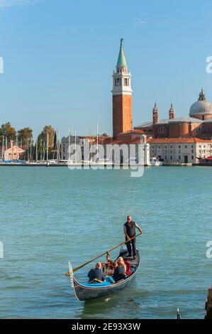 Touristes appréciant une promenade en gondole avec l'île de San Giorgio Maggiore et la basilique dans le fond, Venise, Italie. Banque D'Images