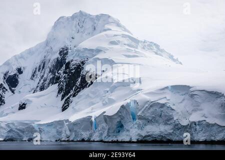 Une montagne de roche noire, ornée d'une épaisse couche de neige éternelle bleuâtre, offre une vue fascinante depuis la mer Banque D'Images