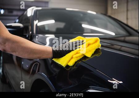 L'homme après le lavage essuie la voiture noire avec un chiffon au lavage de voiture. Main mâle et carrosserie de voiture de près. Banque D'Images