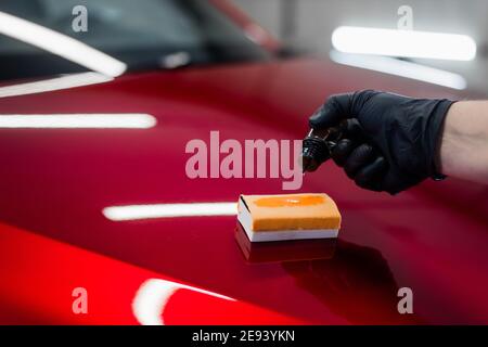 Gros plan d'un revêtement liquide goutte-à-goutte manuel sur un applicateur éponge sur un capot de voiture. Préparation de l'application d'un revêtement spécial sur la surface d'une voiture. Banque D'Images