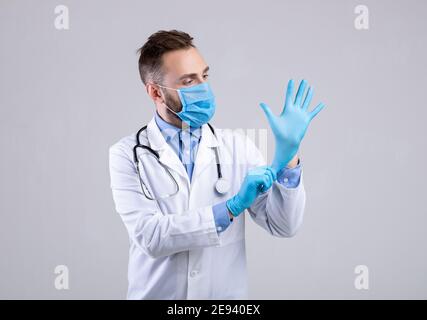 Médecin professionnel en masque médical mettant des gants sur fond gris studio. Prévention des maladies virales Banque D'Images