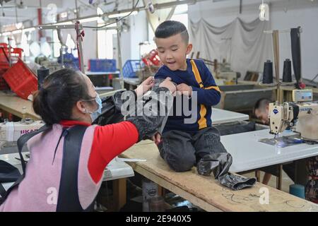 (210202) -- FUZHOU, le 2 février 2021 (Xinhua) -- Congcong, fils de Huang Hailong, tente sur un manchon protecteur que sa mère a fabriqué pour sa grand-mère dans une usine de vêtements de Shishi, dans la province de Fujian, dans le sud-est de la Chine, le 26 janvier 2021. Suite à la résurgence sporadique des cas de COVID-19, de nombreux endroits en Chine ont encouragé les résidents et les travailleurs migrants à rester mis en place pour célébrer le Festival du printemps, pour réduire le flux de personnel et freiner la propagation du coronavirus pendant la période des fêtes. Huang Hailong, un travailleur migrant de Shishi, a déclaré que ce serait sa première fois au cours des dernières années à passer le Banque D'Images