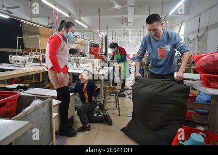 (210202) -- FUZHOU, 2 février 2021 (Xinhua) -- Congcong, fils de Huang Hailong, accompagne ses parents dans une usine de vêtements de Shishi, dans la province de Fujian, dans le sud-est de la Chine, qui prépare des cadeaux pour leurs proches, le 26 janvier 2021. Suite à la résurgence sporadique des cas de COVID-19, de nombreux endroits en Chine ont encouragé les résidents et les travailleurs migrants à rester mis en place pour célébrer le Festival du printemps, pour réduire le flux de personnel et freiner la propagation du coronavirus pendant la période des fêtes. Huang Hailong, un travailleur migrant de Shishi, a déclaré que ce serait sa première fois au cours des dernières années à passer le Banque D'Images