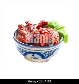 Bol de délicieuses tomates séchées espagnoles recouvertes d'huile feuille de basilic isolée sur fond blanc Banque D'Images