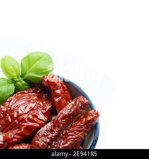 Image partielle de délicieuses tomates séchées espagnoles au soleil dans un foyer sélectif recouvert d'huile de feuilles de basilic isolées sur un blanc arrière-plan Banque D'Images