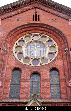 Croix au centre d'une fenêtre circulaire ornée dans une église en brique rouge Banque D'Images