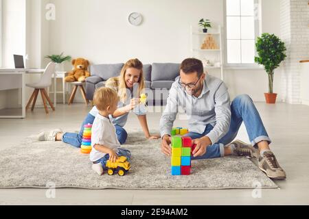 Maman et papa jouent avec leur fils à la maison avec une variété de jouets et de cubes colorés assis dans une pièce. Banque D'Images