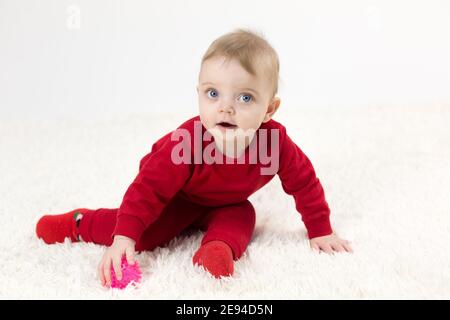 Un petit enfant avec un jouet dans sa main joue sur le sol. Banque D'Images