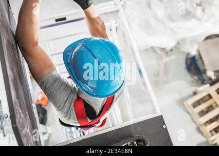 Entrepreneur en construction travailleur portant une protection de tête bleue pour casque dur grimpant sur un échafaudage. Vue de dessus. Thème de l'industrie de la construction. Banque D'Images