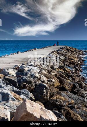 Couple se promenant le long d'une jetée rocheuse au bord de la mer sur l'une des plages de Benalmádena par une journée d'hiver nuageux. Banque D'Images