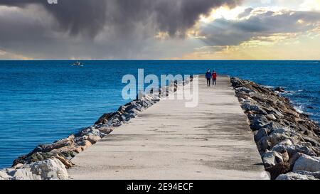 Couple se promenant le long d'une jetée rocheuse au bord de la mer sur l'une des plages de Benalmádena par une journée d'hiver nuageux. Banque D'Images