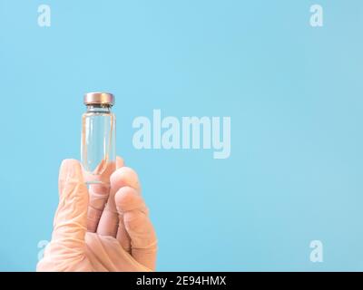 Flacon avec vaccin en main dans des gants médicaux sur fond bleu arrière-plan Banque D'Images