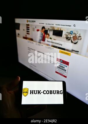 Personne tenant un téléphone portable avec le logo d'entreprise de la compagnie d'assurance allemande HUK-Coburg sur l'affichage en face de la page Web. Mise au point sur l'écran du téléphone portable. Banque D'Images