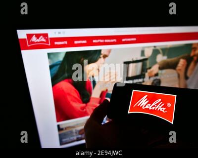 Personne tenant un téléphone portable avec le logo d'affaires de la société allemande de vente de café Melitta sur l'affichage en face de la page Web. Mise au point sur l'écran du smartphone. Banque D'Images