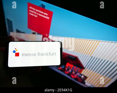 Personne tenant un téléphone portable avec le logo de la société allemande de foire Messe Frankfurt GmbH sur présentation avec la page web d'affaires. Mise au point sur l'écran du téléphone. Banque D'Images