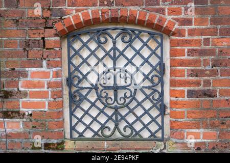 Treillis forgé avec motif sur la fenêtre fermée d'un arrière en brique rouge antique. Architecture de l'Europe médiévale. Banque D'Images