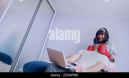 Jeune couple s'amusant dans la chambre. Une femme qui pointait son petit ami au visage avec des gants de boxe. Photo de haute qualité Banque D'Images