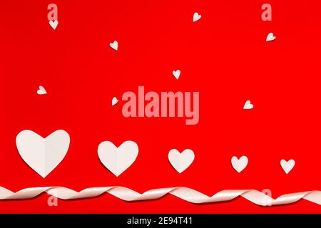 Coeurs en papier blanc avec ruban blanc sur fond rouge et pose à plat. Composition de la Saint-Valentin. Concept de vacances. Banque D'Images