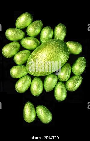 Pile ou groupe de plusieurs couleurs et de différentes tailles d'oeufs de pâques au chocolat enveloppés de papier d'aluminium coloré dans le pastel et le vert lime avec un gros oeuf vert. Banque D'Images