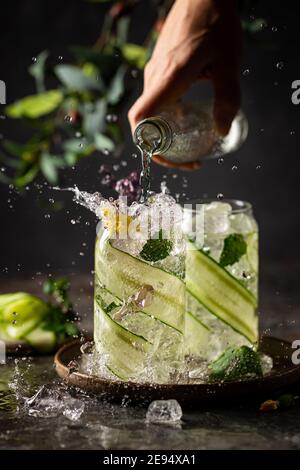 Concombre perfusé de l'eau de détox avec de la menthe dans un verre avec de la glace. Lévitation de boisson de concombre sur fond sombre Banque D'Images