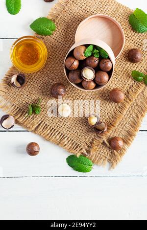 Noix de macadamia en coquille avec feuilles de menthe et miel arrière-plan en bois Banque D'Images