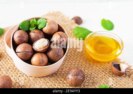 Noix de macadamia en coquille avec feuilles de menthe et miel arrière-plan en bois Banque D'Images
