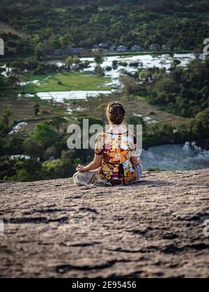 Jeune femme caucasienne assise et méditant sur le sommet du Rock Pidurangala. De l'arrière. Sri Lanka, Asie. Banque D'Images