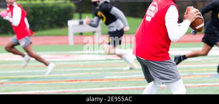 Mise au point sélective sur le quarterback avec le récepteur et le défenseur flou en arrière-plan pendant un match de football rapide de sept sur sept. Banque D'Images